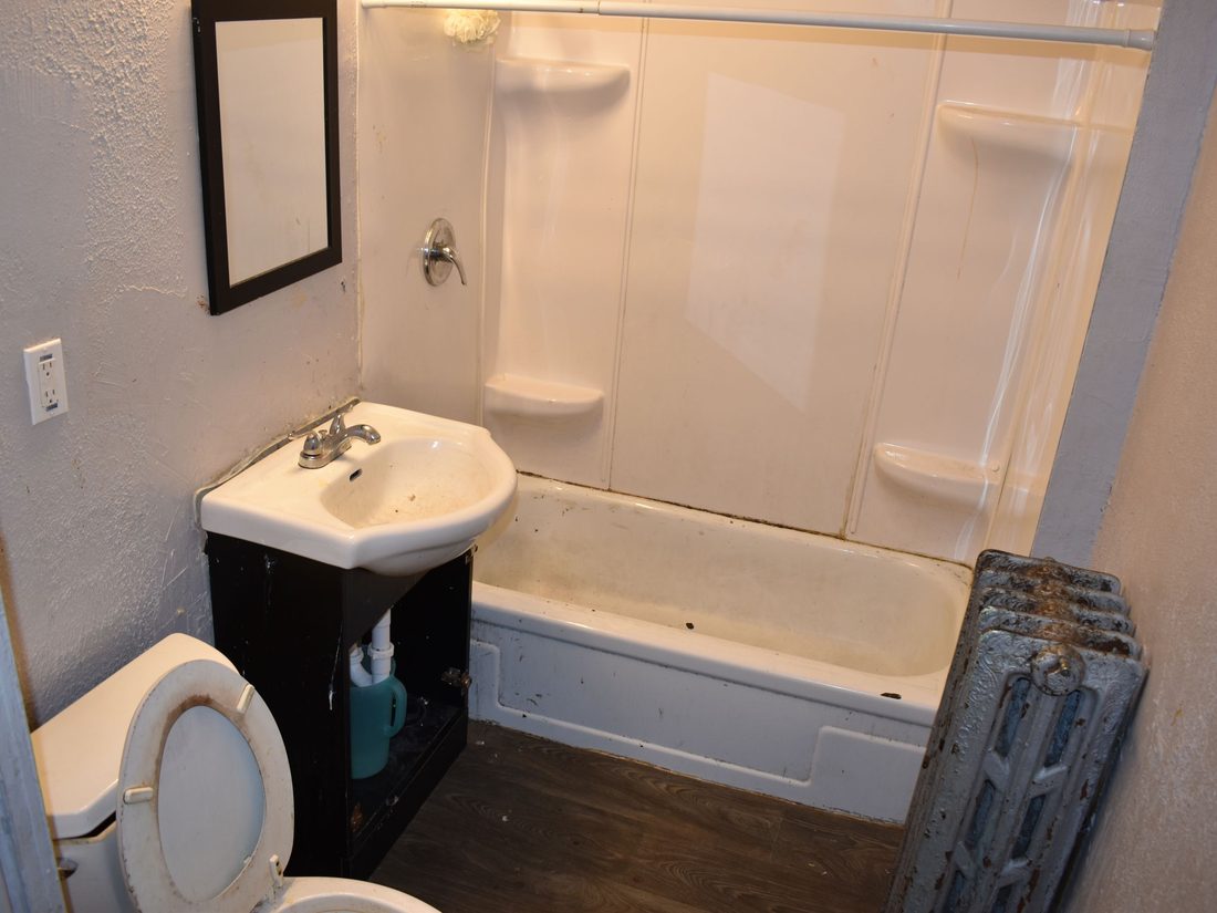 Dated main-floor bathroom with a worn tub and pedestal sink before renovation